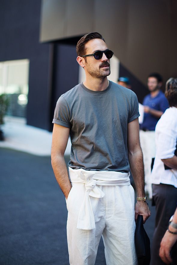 Casual street style look featuring a man in a grey t-shirt and white high-waisted pants tied with a fabric belt.