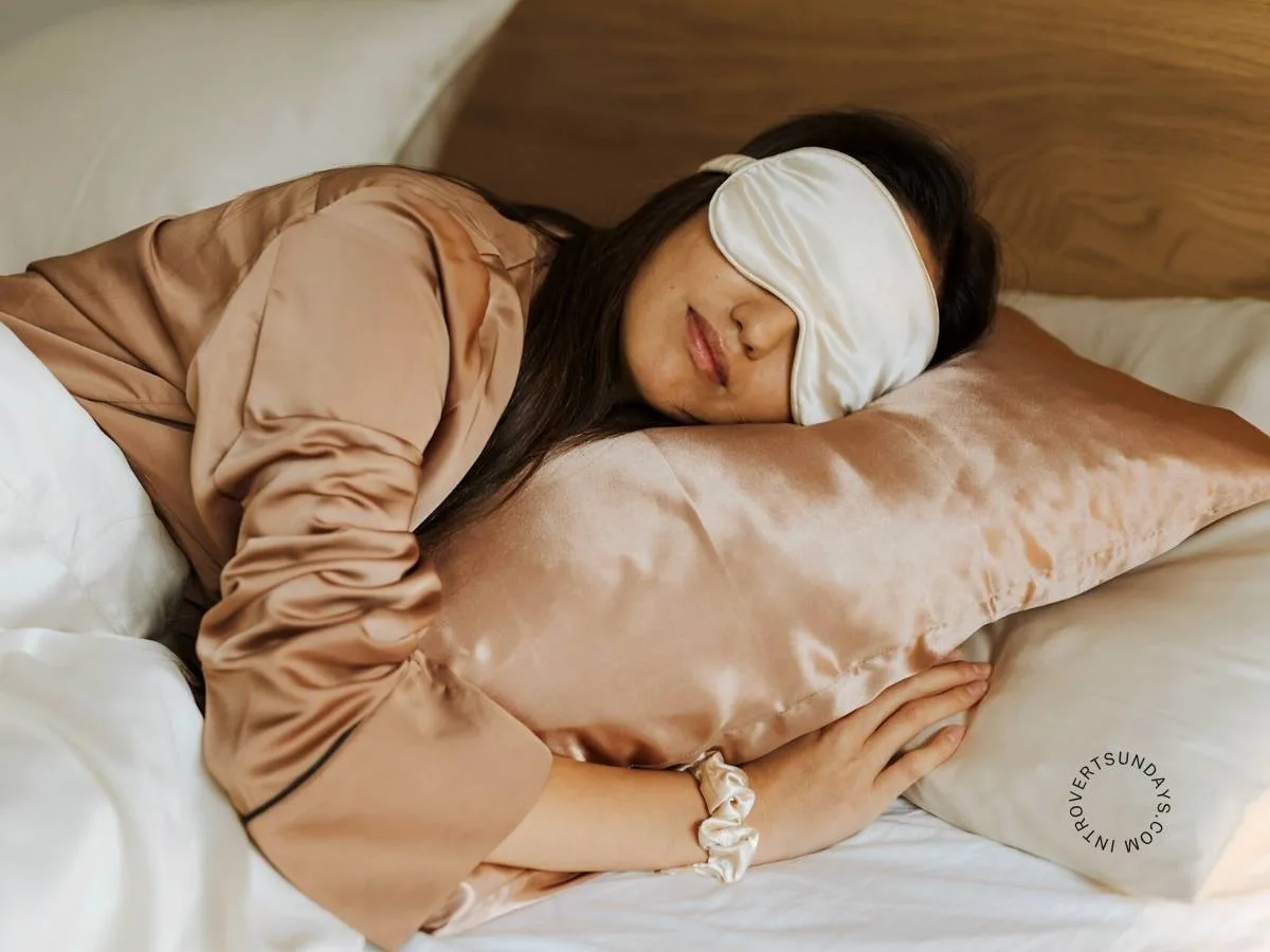 A woman sleeping peacefully on a silk pillow while wearing a sleep mask and satin sleepwear