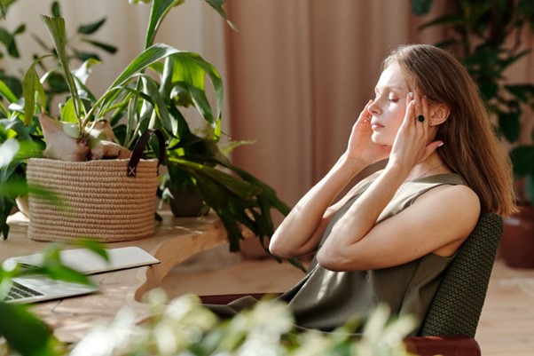 Woman practicing mindfulness meditation at a desk surrounded by green indoor plants