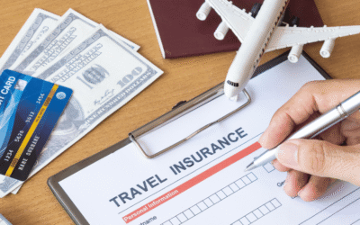 Travel Insurance – Necessary for every journey Hand filling out a travel insurance form with credit card, passport, dollars, and airplane model on desk.