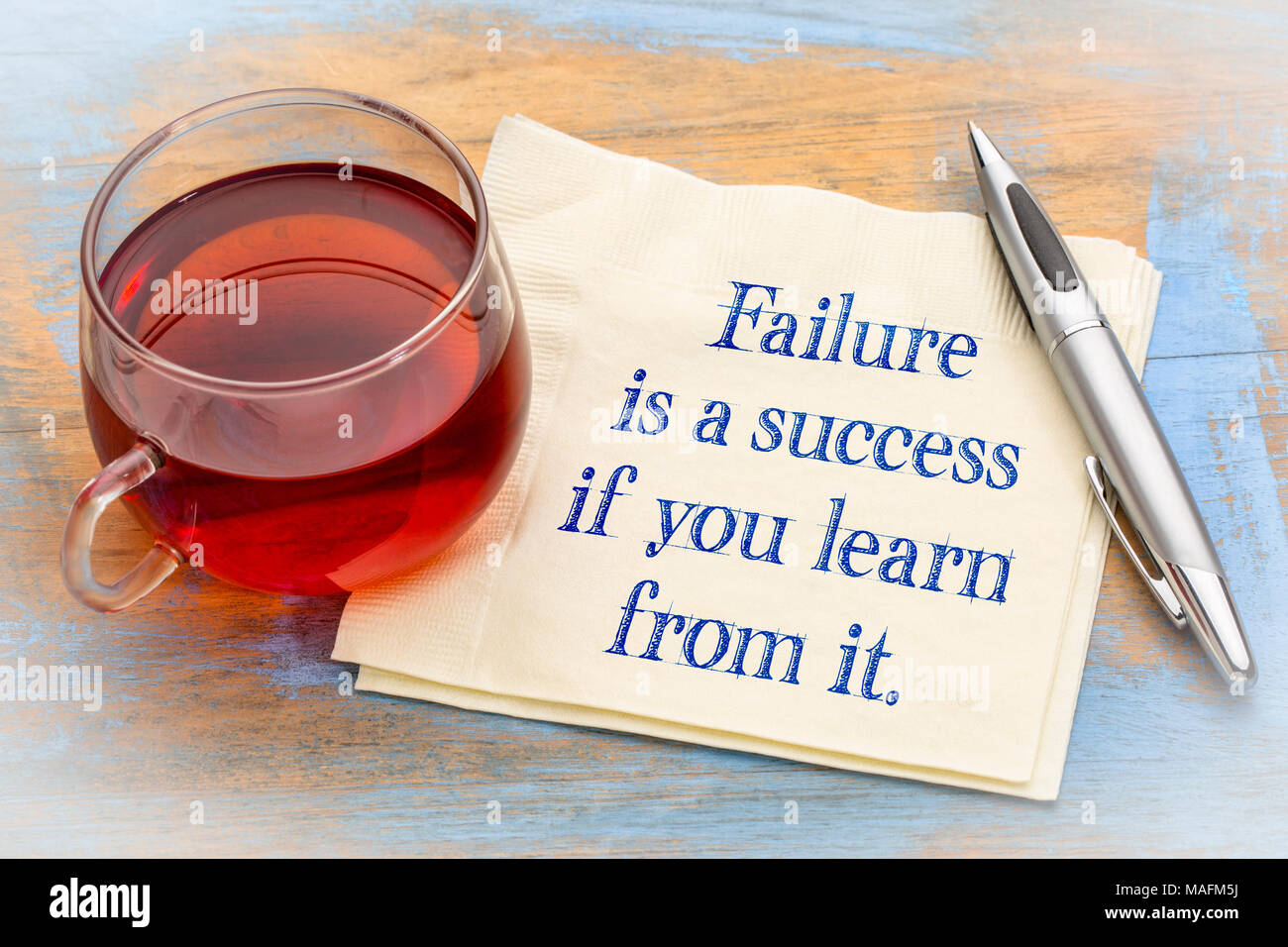 A cup of tea beside a napkin with the motivational quote 'Failure is a success if you learn from it' written on it."