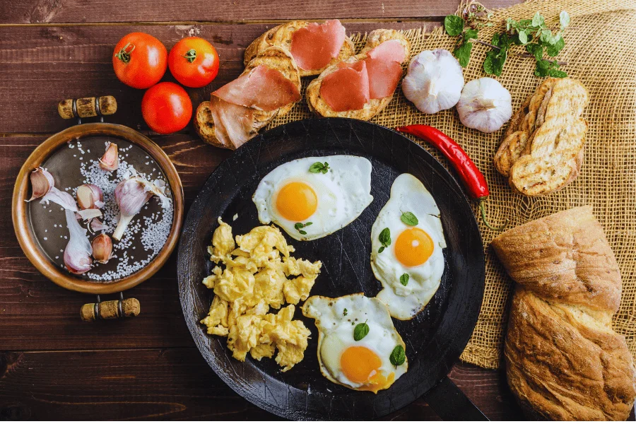 Fried and scrambled eggs with toasted bread, garlic, tomatoes, and herbs on a rustic wooden table a healthy high protein breakfast.