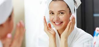 Smiling woman applying cream under her eyes while looking in the mirror.
