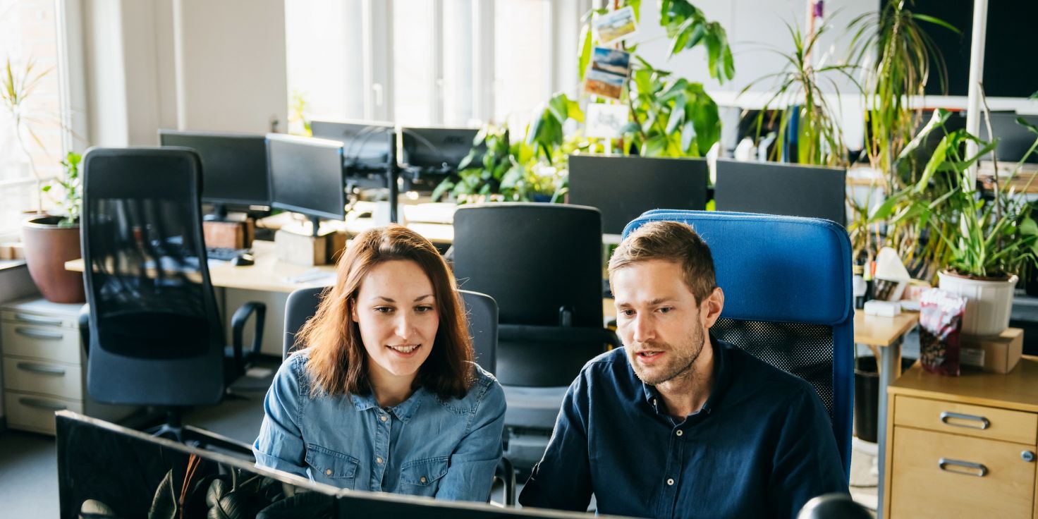 Two people collaborating on a computer in a modern office, representing a small business startup with zero budget
