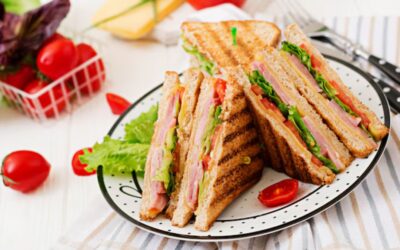 Grilled club sandwiches with lettuce, tomato, ham, and cheese, served on a white plate with cherry tomatoes on the side.