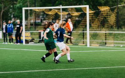Importance of Sports in Daily Life Two female soccer players competing near the goal on a green turf field during a match