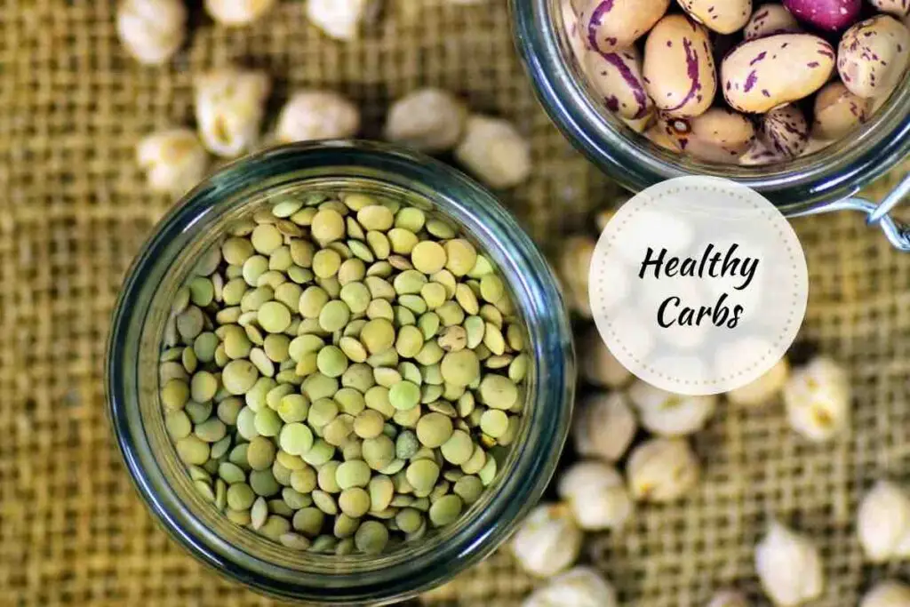 Healthy carbs including lentils, beans, and chickpeas in glass jars on a burlap surface.