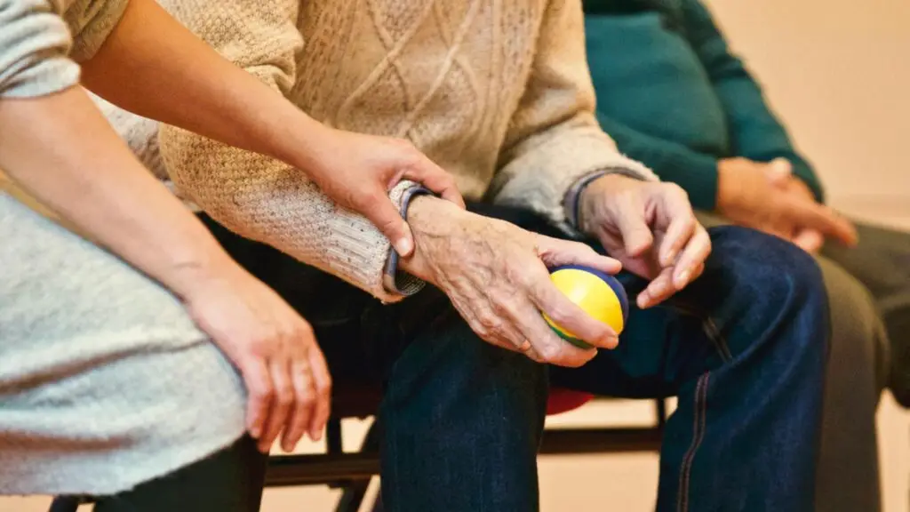 A caregiver offering support to an elderly person during a health care session.