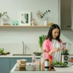Woman preparing a healthy smoothie with fresh fruits and spinach in a modern kitchen for clean eating recipes.